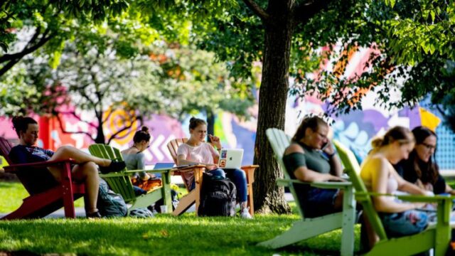 students sitting in colorful adirondack chairs on the grass at centennial common