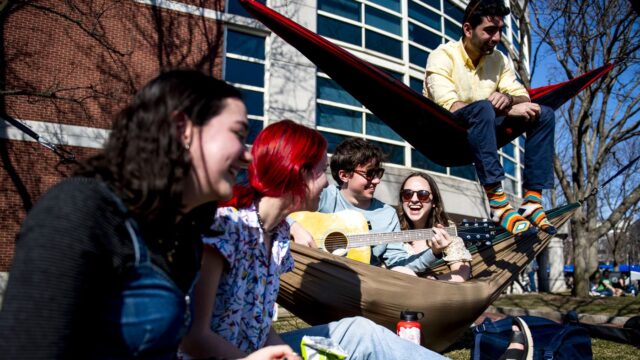 Students enjoy a sunny day in Centennial Common while laughing and playing an acoustic guitar