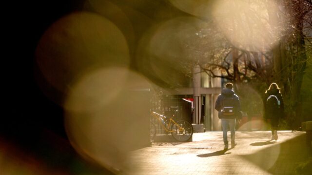 A shot of students walking through campus. The bodies are framed in a sepia-toned bokeh effect.