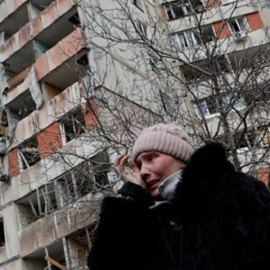 Picture depicts a mourning woman in front of a building damaged by Russian missiles.