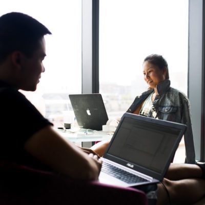 Image of two people on laptops in front of a glass window looking at their screens