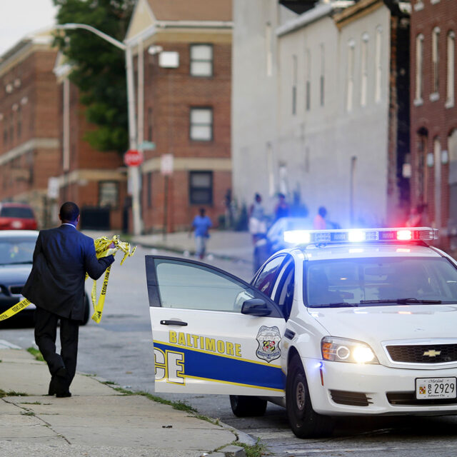 In this July 30, 2015 picture, a member of the Baltimore Police Department removes crime scene tape from a corner where a victim of a shooting was discovered in Baltimore.