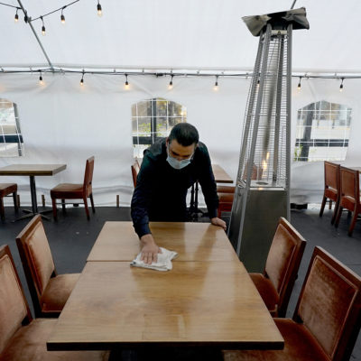 Fabian Rodriguez cleans a table in an outdoor tented dining area of Tequila Museo Mayahuel restaurant, in Sacramento, Calif., Thursday, Nov. 19, 2020.