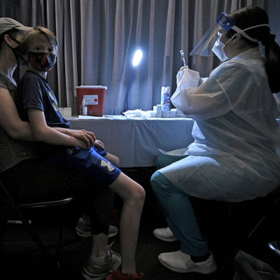 William Barefoot, 13, sits on his mother's lap, Kathleen Barefoot, as a registered nurse fills a syringe with a dose of the Pfizer COVID-19 vaccine for his first shot, at a vaccination site set up in the American Museum of Natural History in New York, NY, May 18, 2021.