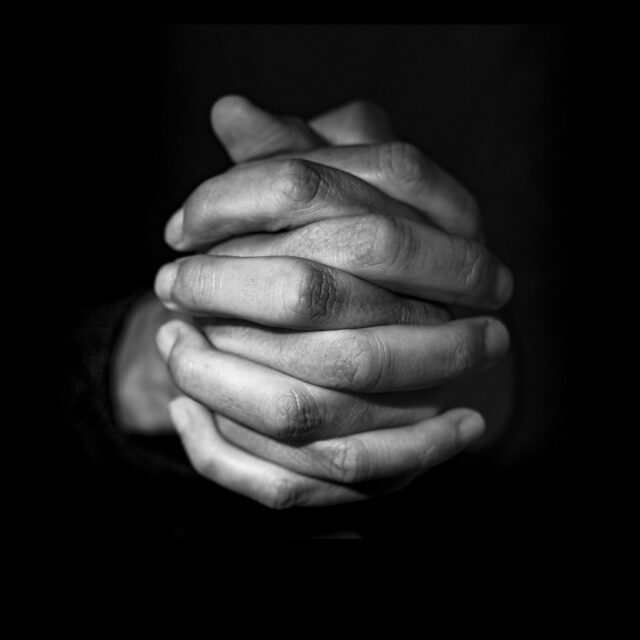 closeup of the hands of a young caucasian man with his hands clasped, in black and white