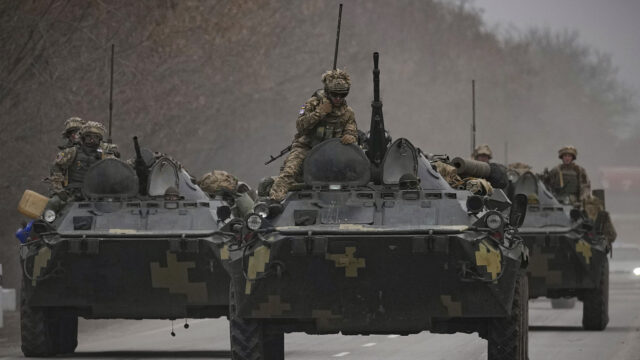 Ukrainian servicemen sit atop armored personnel carriers driving on a road in the Donetsk region, eastern Ukraine, Thursday, Feb. 24, 2022.