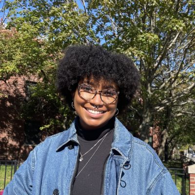 A picture of Jenia, in a denim jacket outdoors as a headshot