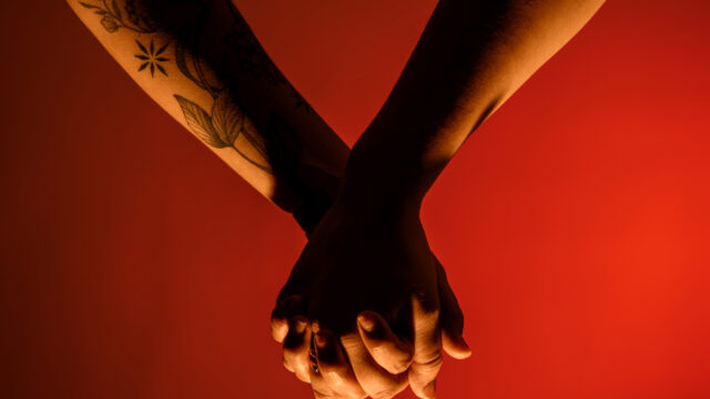 Two hands holding in front of a red background.