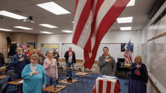 People in a classroom standing up for the Pledge of Allegiance.