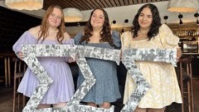Tiffany Pottenburgh (middle) posing with fellow sorority members of Sigma Sigma Sigma. They are holding greek letter signs.