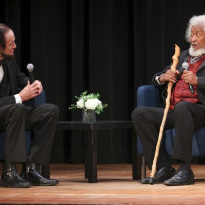Steve Wood portraying Abraham Lincoln and Michael Crutcher portraying Frederick Douglass at the Defending Democracy forum in Lynn. The two are seated and talking.