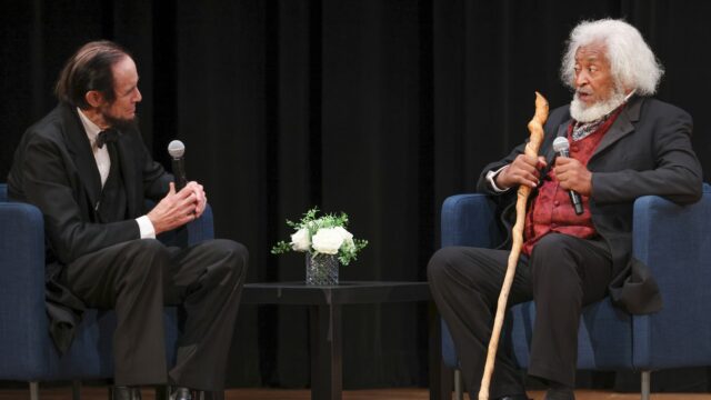 Steve Wood portraying Abraham Lincoln and Michael Crutcher portraying Frederick Douglass at the Defending Democracy forum in Lynn. The two are seated and talking.