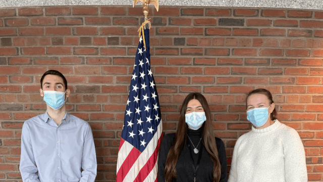 Gianna (middle) and two other co-ops (left and right) posing next to the American flag,.