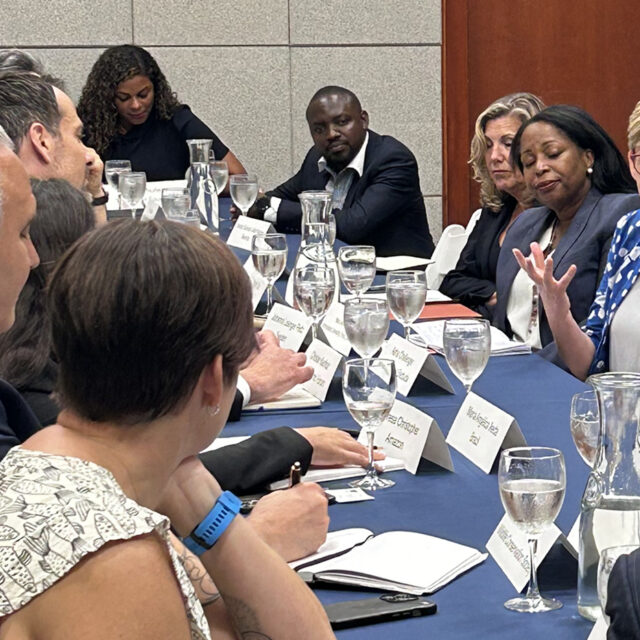 Maria Ivanova in conversation at the first roundtable of End Plastic Pollution International Collaborative. Several people are seated around the table, and are listening attentively.