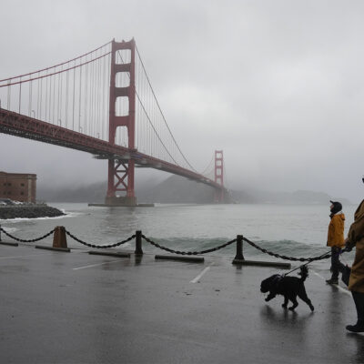 People walk their dogs during a break between rain showers near the Golden Gate Bridge and Fort Point in San Francisco, Tuesday, Dec. 19, 2023. (AP Photo/Eric Risberg)