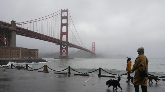 People walk their dogs during a break between rain showers near the Golden Gate Bridge and Fort Point in San Francisco, Tuesday, Dec. 19, 2023. (AP Photo/Eric Risberg)