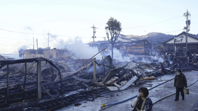 People walk past burn-out marketplace following earthquake in Wajima, Ishikawa prefecture, Japan Tuesday, Jan. 2, 2024. A series of powerful earthquakes in western Japan damaged homes, cars and boats, with officials warning people on Tuesday to stay away from their homes in some areas because of a continuing risk of major quakes and tsunamis. (Kyodo News via AP)