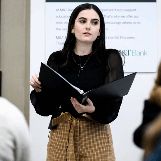 image of andie weiner presenting to audience with folder in hand