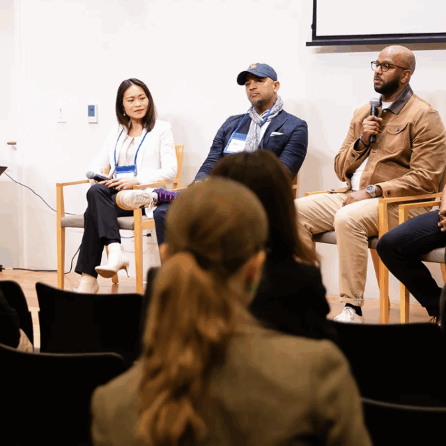 image of 5 convention panelists speaking to each other and audience on stage in wooden chairs