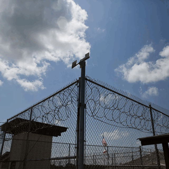 image of barbed wire fence outside prison with sunny sky with two clouds above