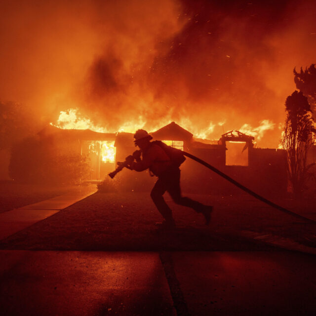 A firefighter battles the Palisades Fire as it burns a structure in the Pacific Palisades neighborhood of Los Angeles, Tuesday, Jan. 7, 2025. (AP Photo/Ethan Swope)