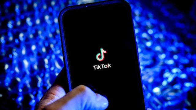 A hand holds a mobile phone with the TikTok logo pictured on the screen.