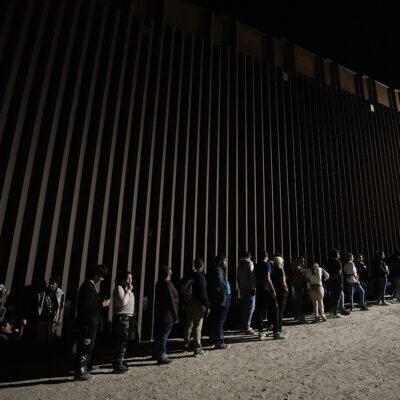 People line up against a border wall as they wait to apply for asylum after crossing the border from Mexico, July 11, 2023, near Yuma, Ariz. (AP Photo/Gregory Bull, File)