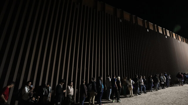 People line up against a border wall as they wait to apply for asylum after crossing the border from Mexico, July 11, 2023, near Yuma, Ariz. (AP Photo/Gregory Bull, File)