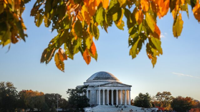 A building is pictured across a body of water at sunset in Washington D.C. (via Unsplash).