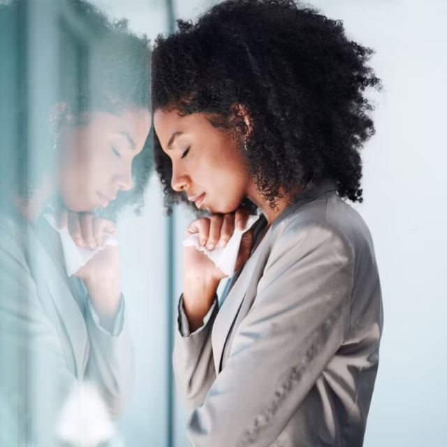 A girl solemnly leans her head against a window.