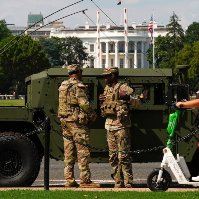 Members of the District of Columbia National Guard patrol in front of the White House as a woman rides past on a scooter