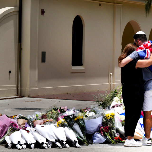 A couple lay flowers at a tribute to shooting victims outside the Bondi Pavilion at Sydney's Bondi Beach, Monday, Dec. 15, 2025, a day after a shooting. (AP Photo/Mark Baker)