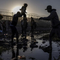 The U.S. is seen in the background as Joiner, a 22-year-old migrant from Venezuela, hands his three-year-old daughter Ivanna to a fellow compatriot as they navigate the riverbed of the Rio Grande while searching for an entry point into the U.S. from along the international boundary between Ciudad Juarez, Mexico, and El Paso, Texas, at sunrise on April 20, 2024. REUTERS/Adrees Latif SEARCH 