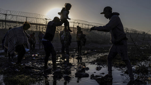 The U.S. is seen in the background as Joiner, a 22-year-old migrant from Venezuela, hands his three-year-old daughter Ivanna to a fellow compatriot as they navigate the riverbed of the Rio Grande while searching for an entry point into the U.S. from along the international boundary between Ciudad Juarez, Mexico, and El Paso, Texas, at sunrise on April 20, 2024. REUTERS/Adrees Latif SEARCH 