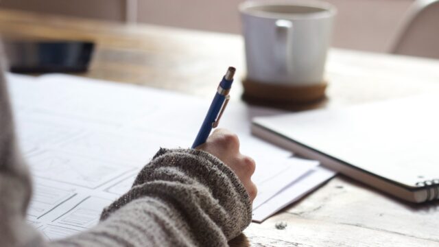A hand is writing on a piece of notebook paper